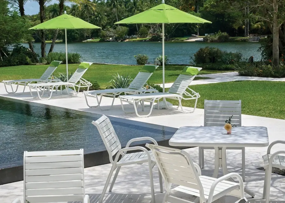 Commercial pool furniture collection featuring white strap chaise lounges, lime green umbrellas, and outdoor dining furniture beside a lakeside pool.